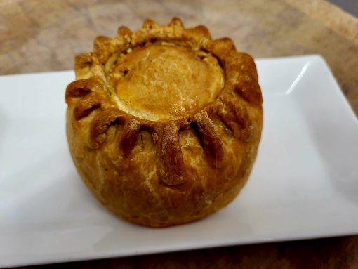 Whole pork pie on a white plate